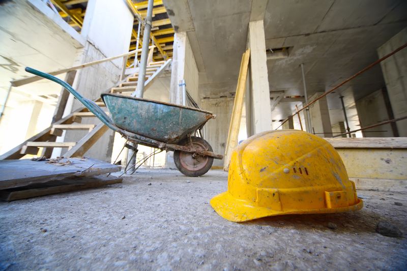 worksite with yellow hard hat and wheelbarrow sat on concrete