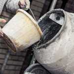 A cement mixer with water being poured in from a white bucket